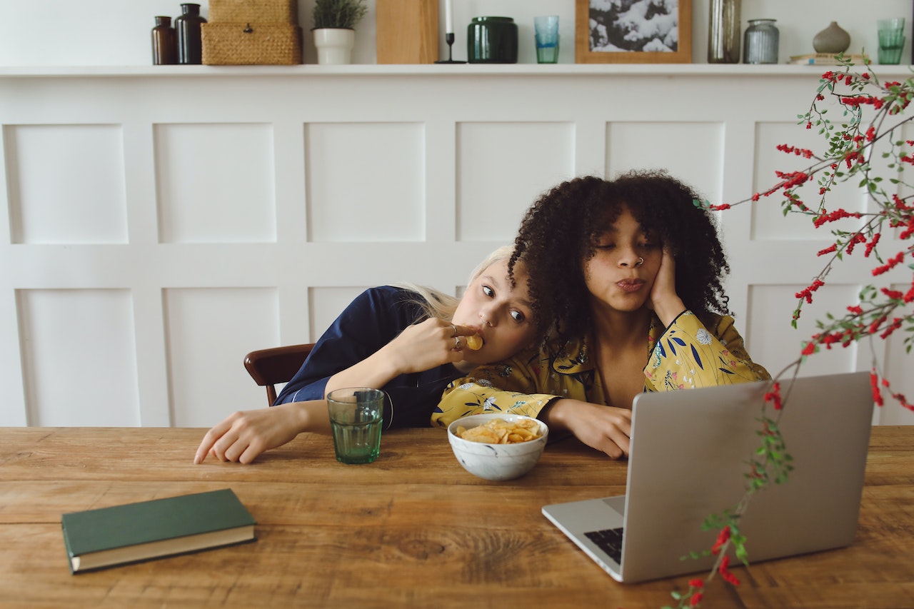 2 young women snacking in front of a laptop
